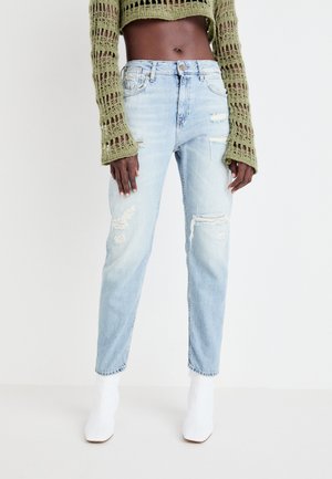 Light blue distressed jeans feature rips and frayed hems, paired with a green knit crop top and white ankle boots.
