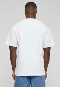 T-shirt en coton blanc à manches courtes, coupe décontractée, col rond, texture lisse, vue arrière unie, porté avec un short en denim bleu.