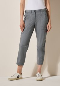 Pantaloni casual grigi a gamba dritta, con due tasche laterali e una tasca con zip. Il tessuto è leggero e dalla texture morbida, abbinati a sneakers bianche.
