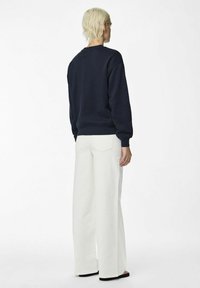 Felpa navy con colletto tondo e polsini a coste, abbinata a pantaloni bianchi a gamba larga. Design semplice, senza motivi o dettagli visibili.