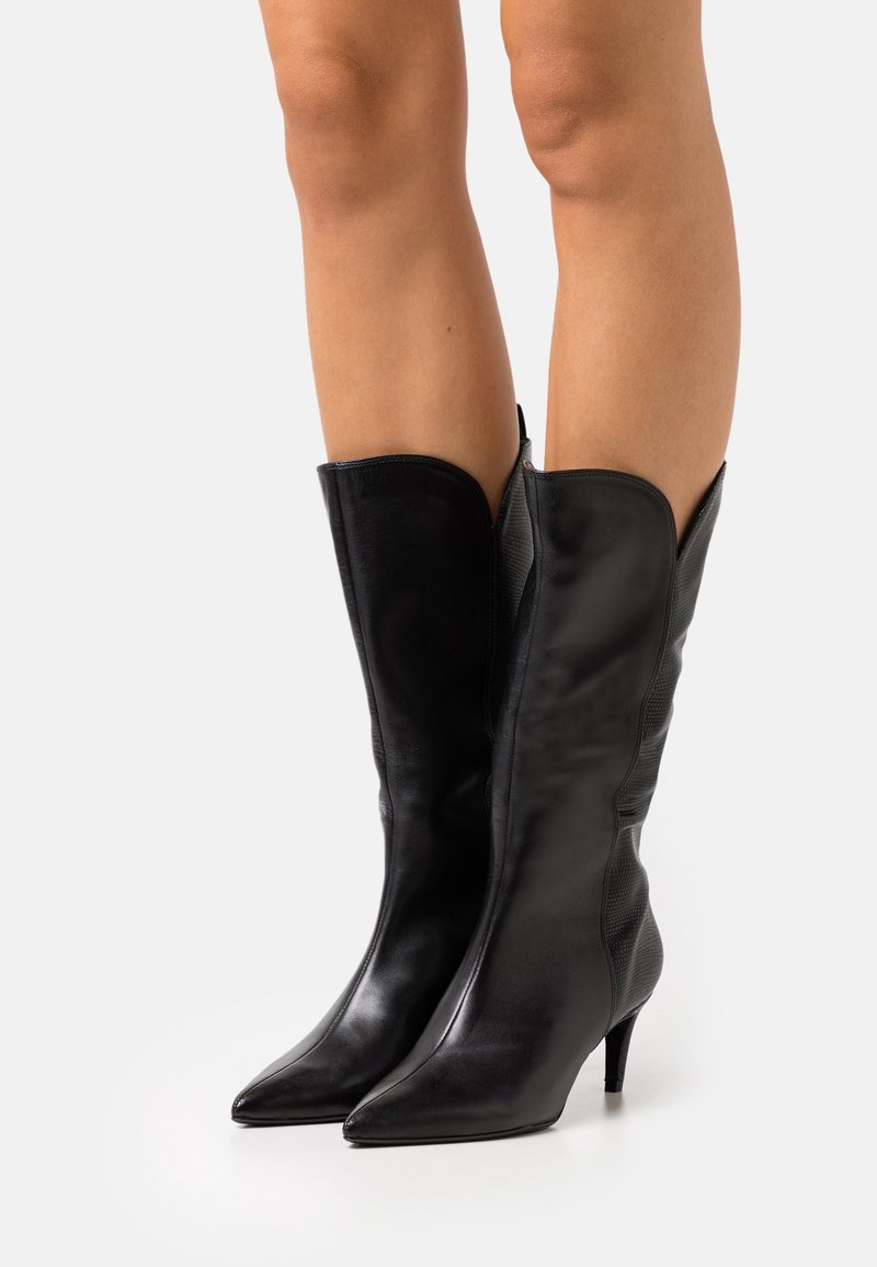 Botas altas de cuero negro hasta la rodilla con punteras afiladas, diseño ajustado y un acabado elegante. Presenta acentos texturizados en los laterales.