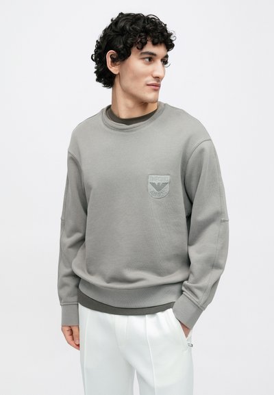 Sweatshirt cinzenta feita de tecido macio, com decote redondo e logotipo bordado no peito. Corte estilo crew com punhos canelados.
