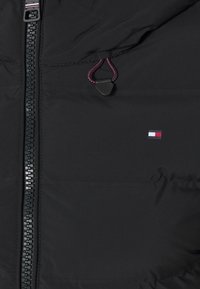 Schwarze Steppjacke mit einem Reißverschluss vorne, rotem und schwarzem verstellbarem Kordelzug und einem kleinen weißen, roten und blauen Logo auf der Brust.