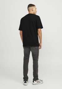Camiseta negra de manga corta combinada con jeans gris oscuro y zapatillas multicolor, vista desde atrás. Diseño simple, ajuste casual.