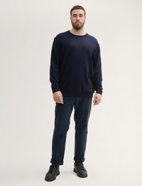 Pull en maille bleu marine avec un col rond, associé à un pantalon bleu foncé et des chaussures noires à lacets. Texture lisse, coupe décontractée.