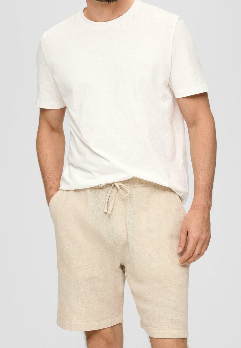 T-shirt blanc en coton léger à manches courtes associé à un short en lin beige avec une taille élastique et un cordon de serrage.