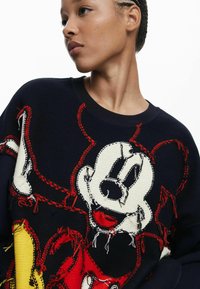 Navyblauer Strickpullover mit einem großen, bunten Mickey-Mouse-Design und roten sowie gelben Akzenten. Sichtbare Nähte sorgen für Struktur.