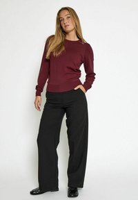 Maglione bordeaux con maniche lunghe, polsini e vita a costine, abbinato a pantaloni neri a gamba larga, indossato con scarpe nere lucide.