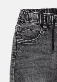 Joggers en denim noir avec une taille élastique, cordon de serrage et poches latérales ; présentent une texture décolorée et des détails de couture contrastants.