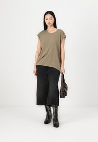 Tricou scurt de culoare verde măsliniu, cu croială lejeră, asortat cu blugi negri cu picioare largi, cizme negre înalte cu detalii albe și o geantă închisă la culoare.