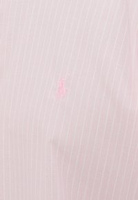 Jasnoróżowa tkanina w cienkie białe paski, z małym różowym haftowanym logo. Gładka tekstura i klasyczny wzór w paski.