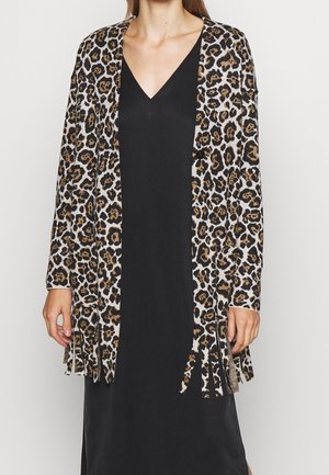 Femme portant une robe noire à col en V avec un long cardigan imprimé léopard avec des détails en franges à l'ourlet et aux manches.