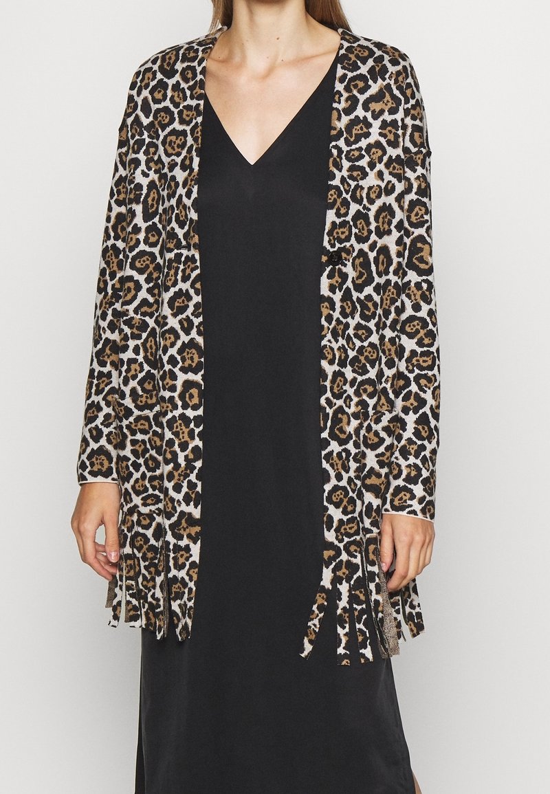 Femme portant une robe noire à col en V avec un long cardigan imprimé léopard avec des détails en franges à l'ourlet et aux manches.