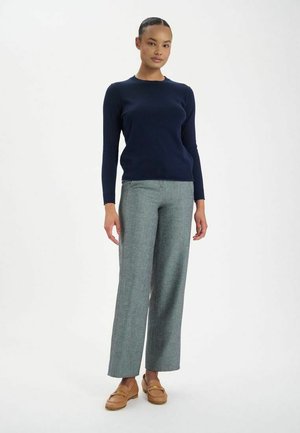 Pull en mailles bleu marine à manches longues associé à un pantalon large gris clair. Des mocassins marron complètent la tenue.