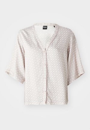 Ljust beige knapplös blus i mjukt tyg med ett geometriskt mönster i off-white. Har korta ärmar och en V-ringning.
