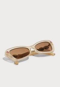 Óculos de sol com armações claras e translúcidas, lentes castanhas e um detalhe em gema rosa nas extremidades externas. Forma slim e angular.