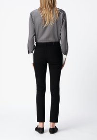 Czarne rurki o gładkim wykończeniu, wysoki stan i pięć kieszeni. Ubranie zestawione z długim szarym topem i czarnymi butami.