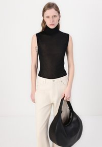 Crni top bez rukava s visokim ovratnikom, uparen s pantalona širokih nogavica boje kreme. Velika crna kožna torba preko ramena s detaljem na zatvaraču.