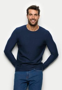 Granatowa koszulka z długim rękawem i okrągłym dekoltem, wykonana z miękkiego materiału, zestawiona z jasnoniebieskimi dżinsami. Brak widocznych wzorów lub akcentów.