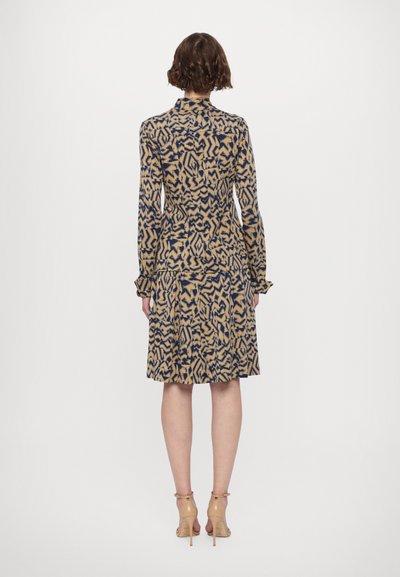 Long-sleeve dress featuring a beige and navy abstract pattern, with a fitted waist and flared skirt. Accentuated sleeves with ruffle detail.