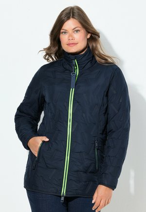 Veste en duvet marine avec un col haut, un motif texturé et des accents de fermeture éclair verts. Elle dispose de poches latérales zippées pour le rangement.