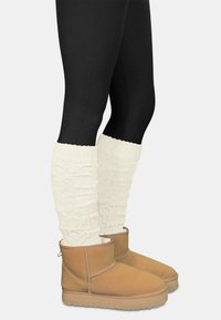 Hellbraune Wildleder-Stiefeletten mit einer Gummi-Sohle, kombiniert mit weißen gestrickten Stulpen, die ein strukturiertes, geripptes Design aufweisen.