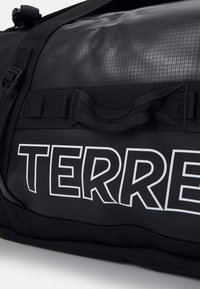 Sac de sport noir en matériau texturé, avec un logo blanc "TERRE" en évidence, des sangles ajustables et une poignée de transport renforcée.