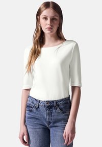 Hvid, kortærmet top i blødt stof, parret med blå højhvide jeans med knaplukning og let falmning.