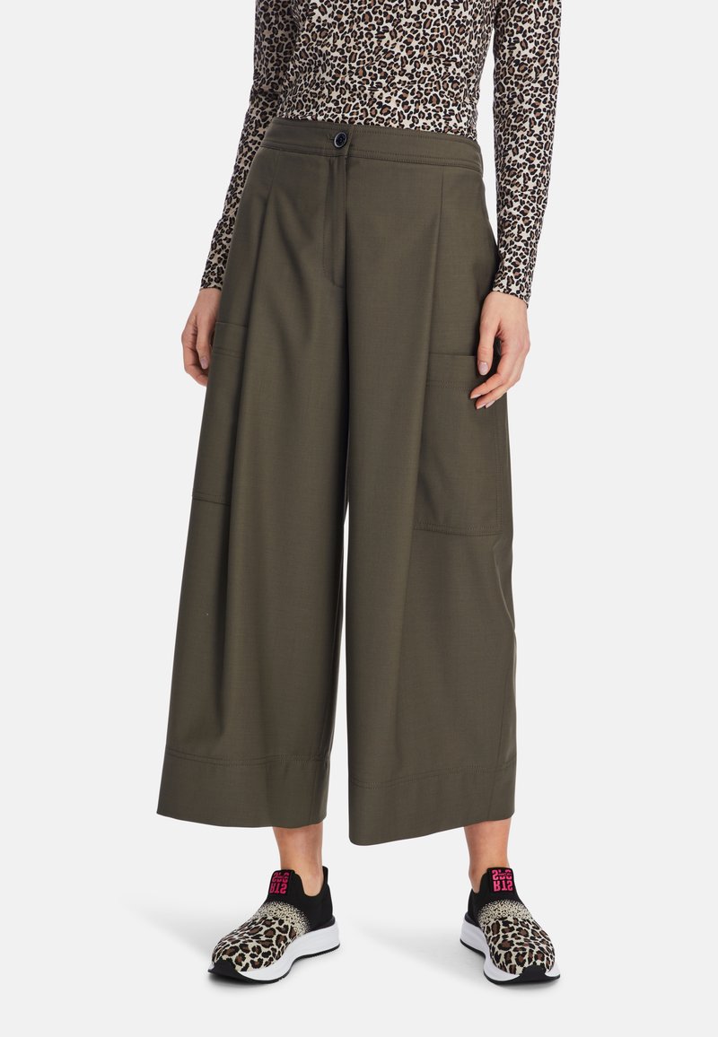 Wide-legged olive green pants made from a smooth fabric, feature two large front pockets, paired with black and leopard print shoes.