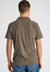 Kortärmad, olivgrön polo av mjukt tyg, med en klassisk krage och en texturerad yta, kombinerad med blå denimjeans.