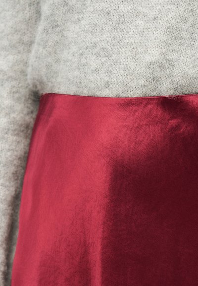 Κοντινή λήψη από ύφασμα κόκκινης σατέν φούστας σε αντίθεση με ύφασμα ανοιχτόχρωμου γκρι πλεκτού πουλόβερ, παρουσιάζοντας την υφή και την αντίθεση μεταξύ των υλικών.