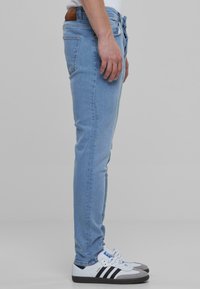 Világoskék, slim fit farmernadrág enyhén elhasználódott textúrával. Öt zsebbel és barna bőr derékpánt címkével rendelkezik. Fehér és fekete cipővel párosítva.