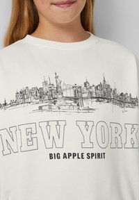 Witte sweatshirt met een zwarte lijntekening van de skyline van New York City, inclusief het Vrijheidsbeeld en de Brooklyn Bridge, met vetgedrukte tekst.