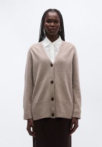 Beežist pehmest kootud materjalist kampsun V-kaelusega, nööbitava esiosaga ja soonikkoes mansettidega; detailiks pruunid nööbid.