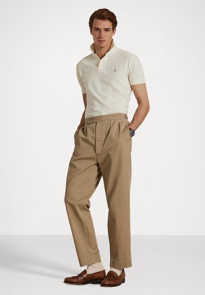 Kremfarget polo skjorte med korte ermer, kombinert med høytlivet beige bukser og brune loafers, med en enkel design og avslappet passform.