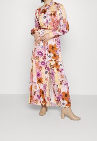 Blomster maxi kjole med krave, lange ærmer, levende nuancer af pink og orange, samt et blødt, svævende stof med sideslids.