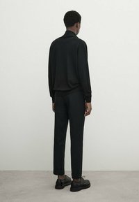 Pull-over en maille noire avec col, assorti à un pantalon noir fuselé ; les deux ont une texture lisse et épousent étroitement le corps.