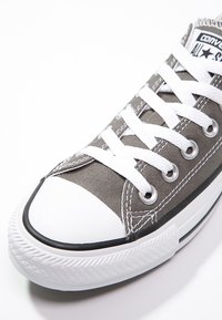 Graue Canvas-Sneaker mit weißer Gummi-Zehenkappe und Sohle, ausgestattet mit weißen Schnürsenkeln und Metallösen. Klassisches Chuck Taylor All-Star Design.