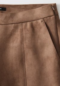 Pantaloni in suede marrone con una superficie liscia, vita piatta e tasche laterali. Presentano linee pulite e dettagli di cucitura minimi.