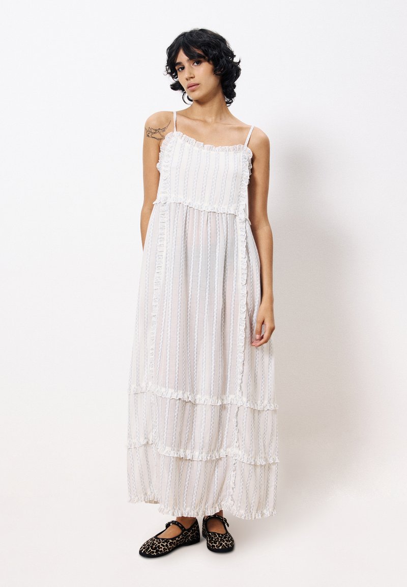 Witte maxi-jurk met gelaagde ruffles, verticale strepen en verstelbare spaghettibandjes, gecombineerd met zwarte flats met panterprint.