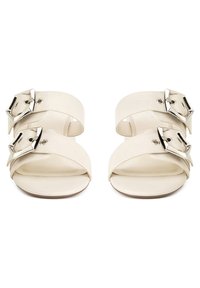 Kremowe sandały z dwoma szerokimi paskami, każdy z dużą srebrną klamrą, płaską podeszwą i odkrytym palcem.