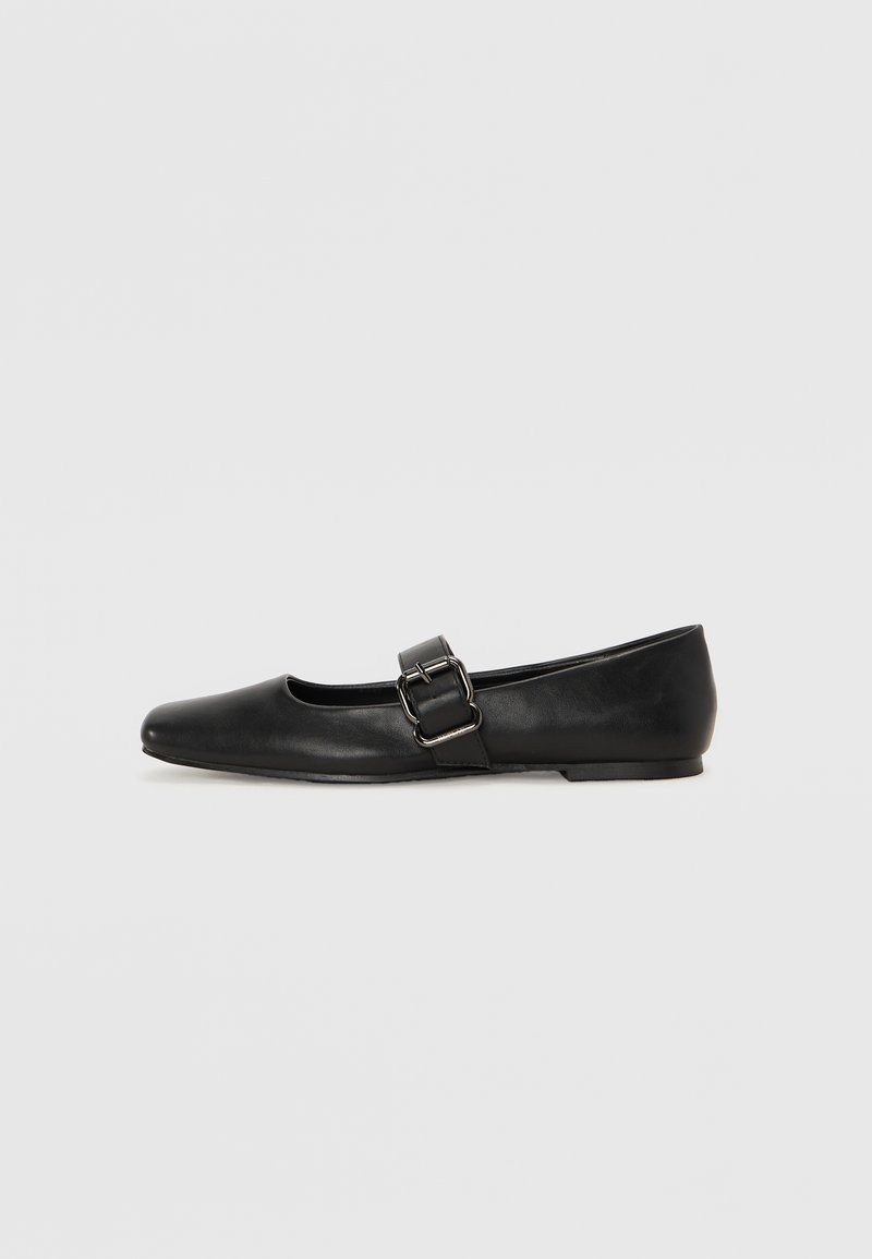 Ballerines en cuir noir avec un bout rond, une sangle latérale à boucle et une semelle plate, présentant une texture lisse et un design minimaliste.