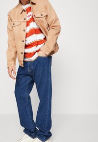 Chaqueta vaquera beige, camiseta de rayas blancas y naranjas, vaqueros azules y zapatillas blancas. Tejido suave, corte holgado, estilo casual.