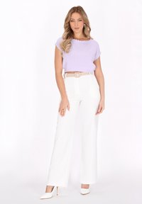 Lilla strikket cropped top med bølgede kanter, parret med hvide vide bukser og et beige bælte, suppleret af hvide spidse hæle.