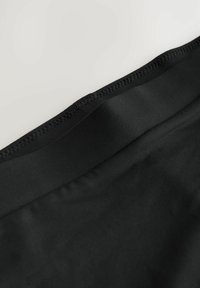 Crni materijal s glatkom teksturom, sa ravnim pojasom i suptilnim šavnim detaljima duž ruba.