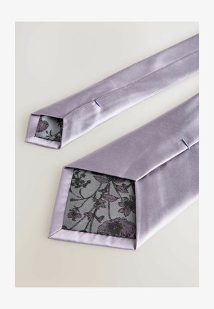 To lilla satinslips med spidse ender, der afslører et blomster mønstret stoffor i indersiden. Glat tekstur med svag glans.