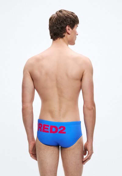 Sinised ujumispüksid, millel on vormitud disain ja suur roosa tekst "RED2" tagaküljel. Sile tekstuur ja elastne vöökoht mugavuse tagamiseks.