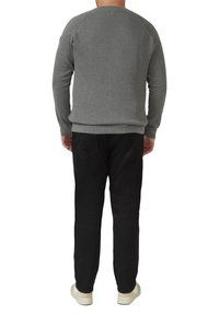 Szary prążkowany sweter z rękawami typu raglan, okrągłym dekoltem i dopasowaną talią, w połączeniu z czarnymi spodniami i białymi trampkami. Widok z tyłu.