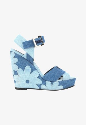 Sandale compensée avec brides en denim et boucle, présentant des motifs floraux bleu clair sur un talon plateforme en denim bleu foncé.