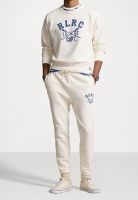 Krämfärgad sweatshirt och joggers med blå grafisk tryck, med ribbade muddar, dragsko i midjan och elastiska hems vid anklarna.